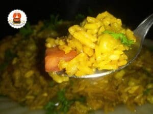 Colher de arroz amarelo com frango, cenoura e ervilhas, decorado com salsinha.