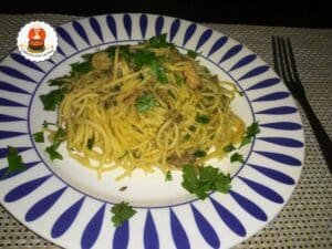 Prato com espaguete envolvido em molho com pedaços de sardinha e cheiro verde.
